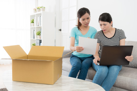 pretty attractive girls received online shopping parcel at home and looking at invoice finding mistake feeling dumbfounded together.の写真素材