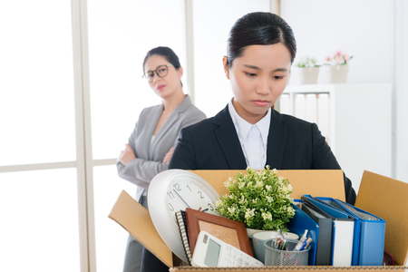 sad pretty office worker girl losing company job packing personal items ready to leave and her manager looking at her feeling happy. selective focus photo.の写真素材