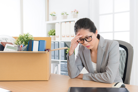 sadness pretty female office worker is fired packing personal belongings sitting on working desk feeling upset and thinking future job.の写真素材