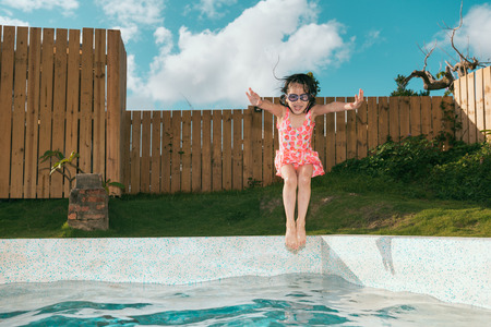cheerful pretty female kid child jumping into swimming pool to play cool water in summer season.