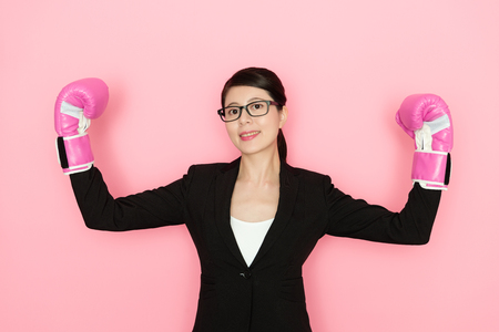 smiling beautiful female office worker wearing boxing showing muscles looking at camera isolated on pink wall background.の写真素材