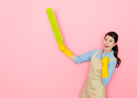 happy beautiful mother finished all housekeeping feeling cheerful standing in pink background and raised feather duster tool face to camera celebrate.の写真素材