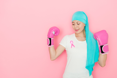 happy beauty girl having cancer problem and wearing boxing gloves decided courage to fight illness isolated on pink background.の写真素材