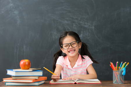 happy cheerful female student doing homework in class on chalkboard background and looking at camera. back to school concept.の写真素材
