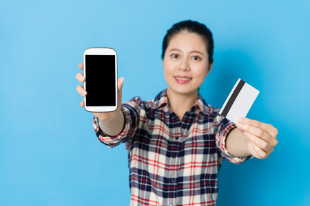 selective photo of confident smiling woman showing mobile pay concept with smartphone with credit card isolated on blue background.の写真素材