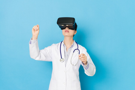 beautiful pretty hospital doctor woman wearing VR technology standing in blue background and viewing 3D simulation video doing surgery work.の写真素材