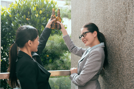 Two happy Asian women celebration successful teamwork cooperation and cheers up the beer bottle outside of office company.の写真素材