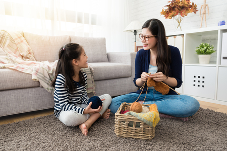 sweet Asian kids stay with her mother and enjoy knitting together sitting on the floor of the living room at home