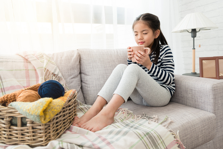 cute Asian kids enjoy and smell hot chocolate happy to drink it sitting on the floor in the living room at homeの写真素材