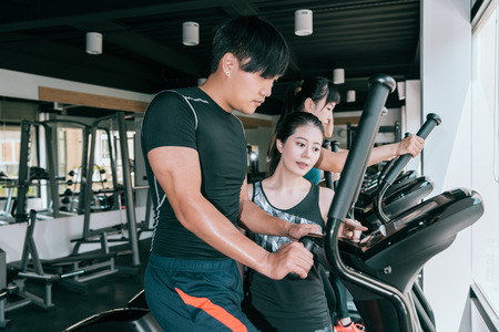 man working out on elliptical machine in gym with his personal trainer. Healthy lifestyle fitness...