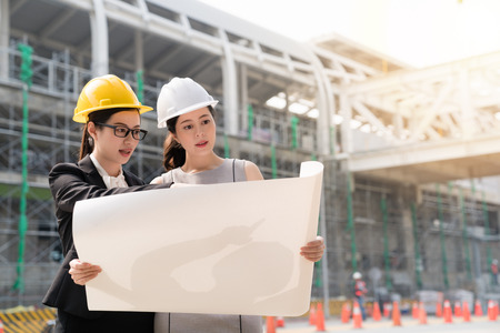 Two female architects in building helmets and safety glasses looking at building construction blueprint. architectural concept discussing with each other. a side view.の写真素材