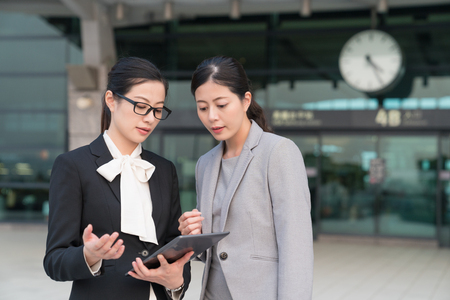 Two asian office lady discussing business by using the tablet outside the high speed rail station.の写真素材