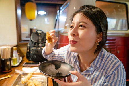 asian woman eating japanese skewer in izakaya. view from closeup. looing happily.の写真素材