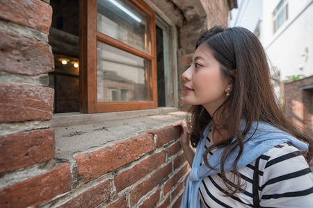 asian woman looking inside through the window. standing at the old house.の写真素材