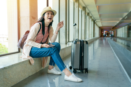 asian visitor laughing and sitting on the window. holding the mobile. view of relaxing and enjoying.の写真素材