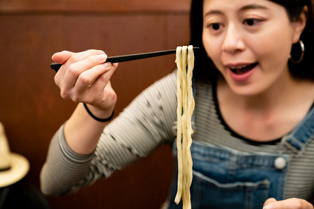 pretty woman smiling and eating japanese udon happily in a ramen shop in osaka of japan.の写真素材