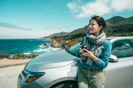 beautiful woman taking pictures for the stunning view and leaning her body on a car.