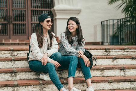 two good friends siiting on the stairs and laughing happily while traveling and hanging out together.の写真素材