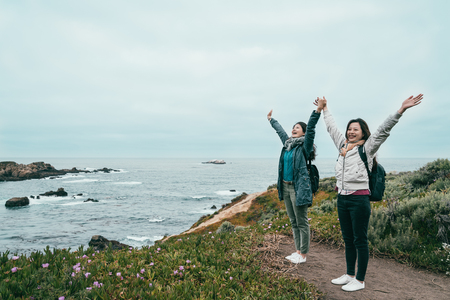 two good friends looking very excited and celebrating with arms raising standing on a beautiful coast.の写真素材