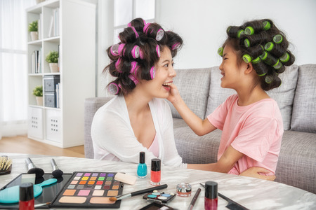 beautiful mom and her lovely kid sitting in the living room with a lot of cosmetics on the table, smile joyfullyの写真素材