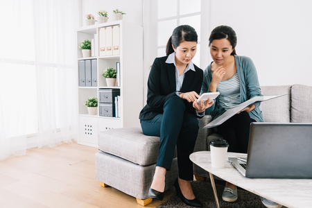 insurance agent and the young girl discussing the insurance plan and counting on calculator. bright home office lifestyle. Female agent consulting clients in living room.の写真素材