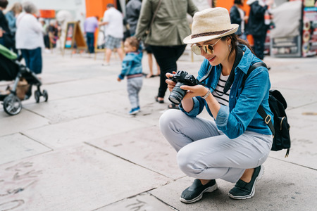 elegant female traveler crouch on the street and taking picture of the ground in a busy street....