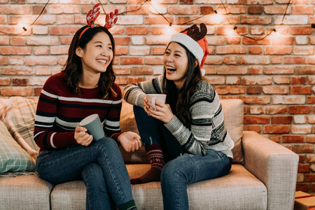 young girls chatting and having fun at home. relaxing celebrating xmas holiday concept. best friends with santa hat and deer cheerful laughing.の写真素材