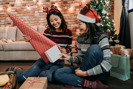 asian young girls having fun wrapping gifts at home. great teamwork of friends packing presents for christmas. prepare for coming up new year and xmas.の写真素材