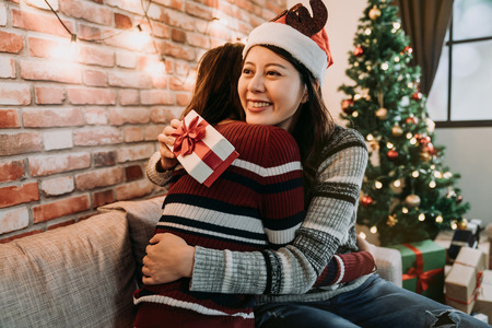 girl best friends celebrating christmas together. young ladies exchanging gifts at home and feel thankful hugging. love friendship on xmas concept.の写真素材