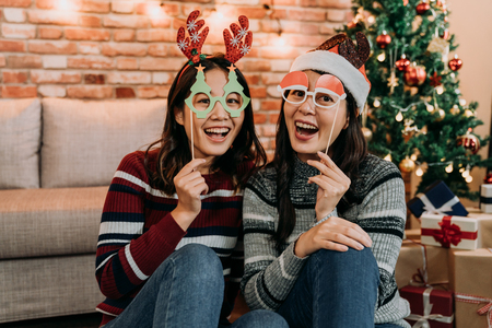 Picture showing two of friends celebrating Christmas at home. young females having fun with fake glasses on face. girlfriends face to camera joyfully smiling.の写真素材