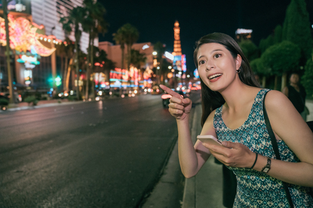 Urban city modern Asian girl using phone app walking on street las vegas, USA. Happy young adult night lifestyle travel in America. attractive lady pointing at the destination.の写真素材