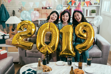 attractive girls celebrating new year eve at home. young friends carrying gold 2019 number balloons cheerfully having fun in house party. asian women indoor lifestyle concept.の写真素材