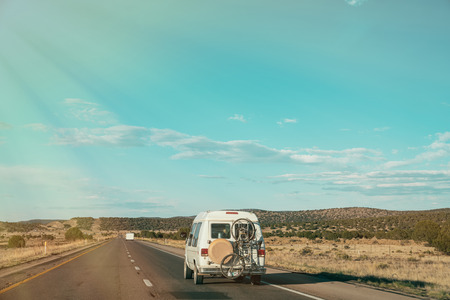 white van driving on the country road with bicycle hanging outside the back. beautiful blue sky and green yellow wild nature view. asphalt highway landscape under good weather on sunny day.の写真素材