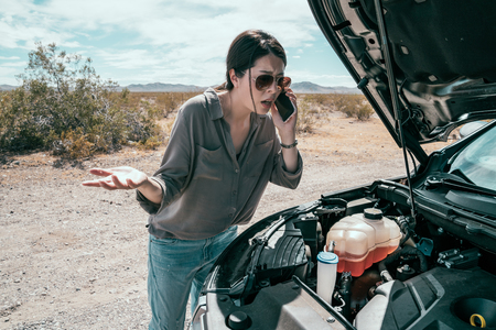 female driver standing on the road on sunny day beside the black car. young woman with sunglasses using cellphone calling for help during the car accident break down on the highway.の写真素材