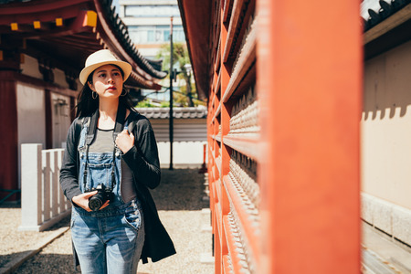 tourist curiously looking at the red praying wall in the temple. young female traveler walking in peaceful path in temple. girl taking trip in osaka attractions alone.の写真素材