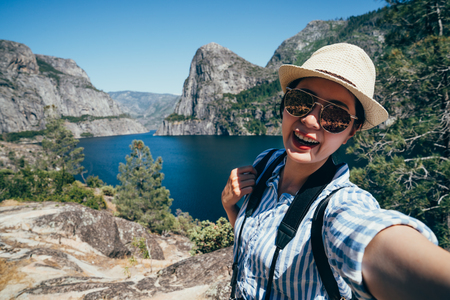 asian backpacker visit yosemite national park cheerfully taking selfie with beautiful nature o shaughnessy dam. young girl tourist attractive smiling traveling in san franisco usa summer vacation.の写真素材