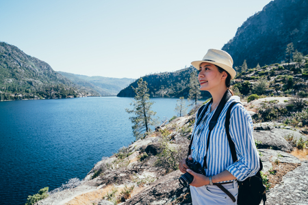 asian girl photographer smiling holding dslr camera sightseeing the nature view of hetch hetchy reservoir. young lady tourist hiking in yosemite national park in travel trip san franisco on sunny day.の写真素材
