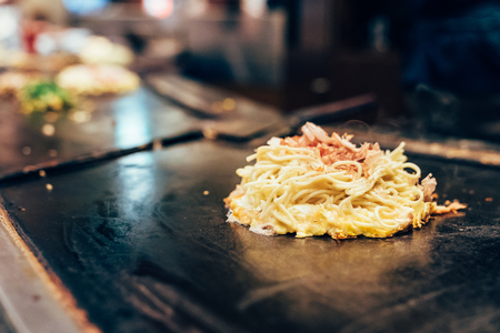 delicious okonomiyaki pancake on teppanyaki pan. hot street food with smoke around on the iron plate. tasty local japanese style cuisine concept.の写真素材
