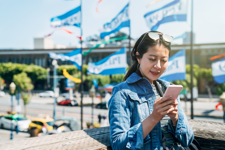 happy woman tourist with sunglasses on head using cellphone cheerfully chatting texting message with friends. young girl looking online map app on mobile phone standing in pier 39 san francisco.の写真素材