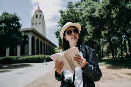 female asian student in sunglasses working and overseas study in university language learning in stanford. college girl abroad holding guided book and camera sightseeing at school in summer vacation.の写真素材