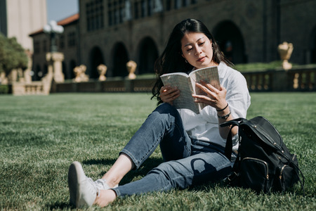 young female asian student reading book at school park in university in america.の写真素材