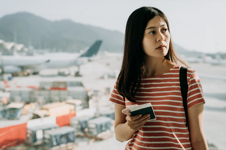 Traveler woman plan and backpack see the airplane at airport glass window. Asian female tourist hold bag and passport board pass near luggage in hall airplane departure. Travel and Holiday Concept.の写真素材