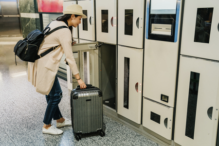 young travel female backpacker putting luggage in coin locker in lobby airport. strong elegant tourist woman in hat holding taking up heavy suitcase open the door. trip on spring holiday.の写真素材