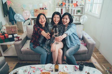 group of happy women cheers toasting glasses wine with colorful confetti all around the decorated room. cheerful ladies clinking champagne celebrating party. presents gift boxes balloons in house.の写真素材