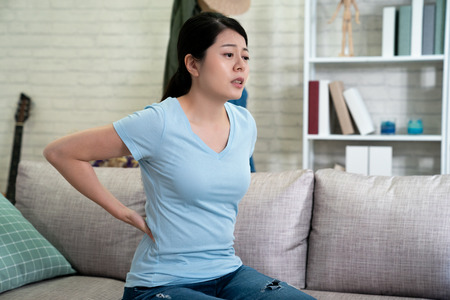 Unhappy asian woman suffering from backache at home.