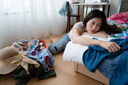 frustrated woman packing luggage in bedroom relaxing on bed with unhappy emotion.の素材 [FY310120650090]