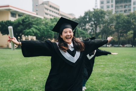 happy asian female students in mortar boards and bachelor gowns with celebrating successful graduation.