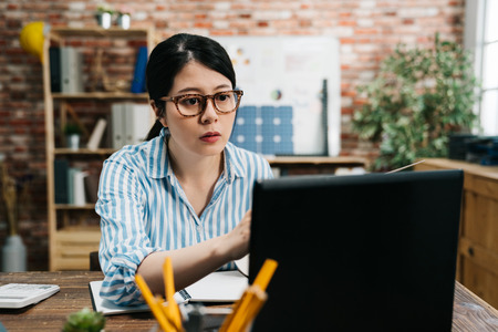 beautiful asian chinese business woman sitting at wooden desk in cozy modern office.の写真素材