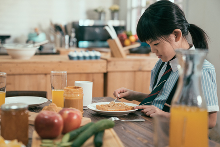 Pretty asian chinese little girl student drinking fresh orange juice with pleasure at kitchen table in the morning.の写真素材