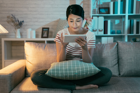 young elegant mother e learning online internet web site study after kid sleep. housewife hard working study on digital tablet stay up late at night in dark living room at home smiling touch screenの写真素材